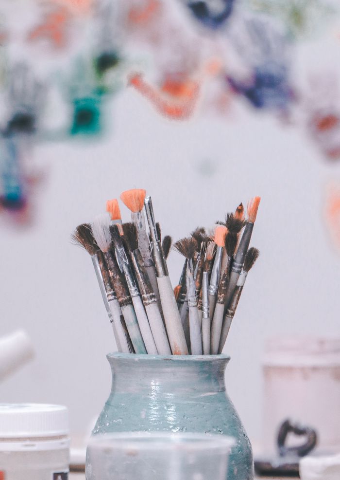 Mastering the First Impression: Your intriguing post title goes here A vibrant collection of paintbrushes in a ceramic vase with blurred colorful art in the background.